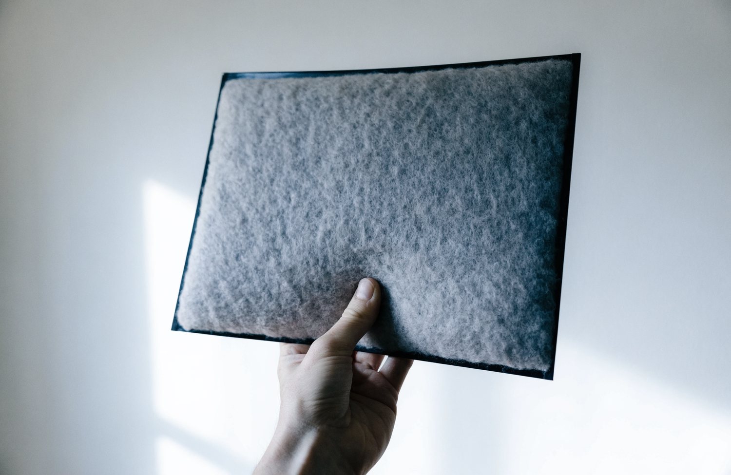 A hand holding up a washable pre-filter screen coated in an even grey layer of household dust.