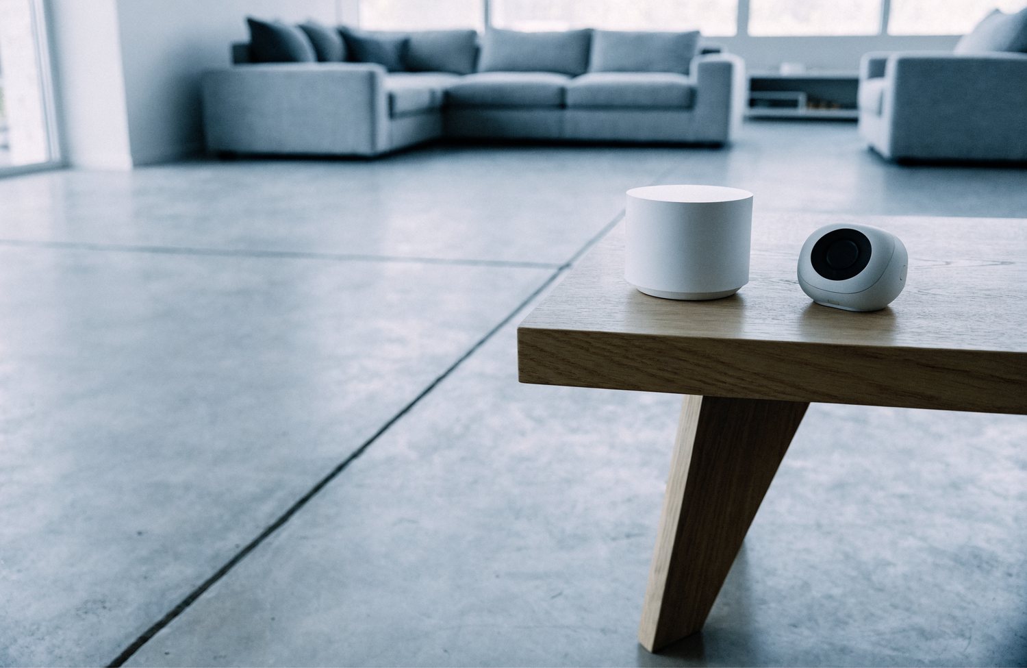 A very small cylindrical desktop air purifier on a side table beside an air quality monitor, in a much larger living room.